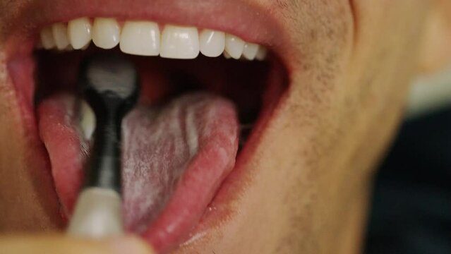 Close up of man brushing his tongue with a manual toothbrush