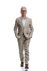 full body picture of elegant man in his 60s walking with hands in pockets