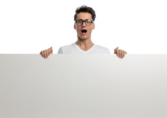 shocked young man with glasses holding empty board and being surprised