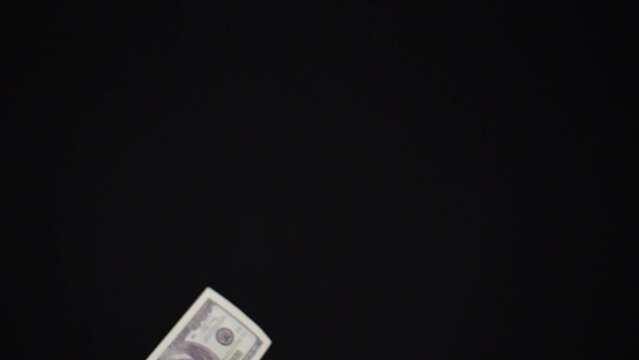 Money dollars fly up in a heap and begin to slowly fall to the bottom. On a black isolated background, one hundred dollar bills are mixed in the air in front of the camera lens.