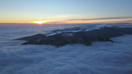 Aerial drone panorama of a winter sunset over Parang Mountains. A sea of clouds is covering the dense pine forests underneath. Evening time, Carpathia, Romania.

