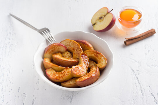 A white bowl of baked apple slices with cinnamon on a light blue background. Delicious homemade vegan dessert