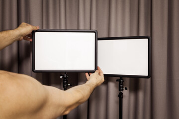 A man hands holds a light panel on a tripod in a home interior. Concept of selfy image.