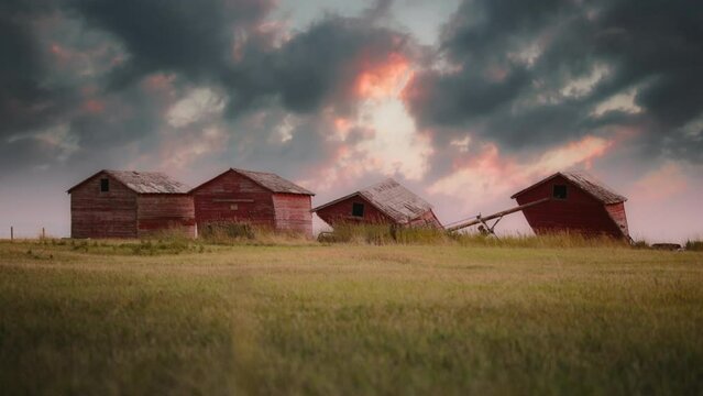 Epic sunset over a row of abandoned old red barns in the field. Slow motion. 