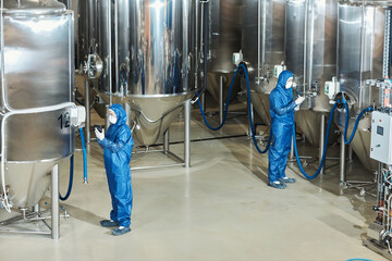 Wide angle view at factory workshop with two workers operating storage tanks - Powered by Adobe