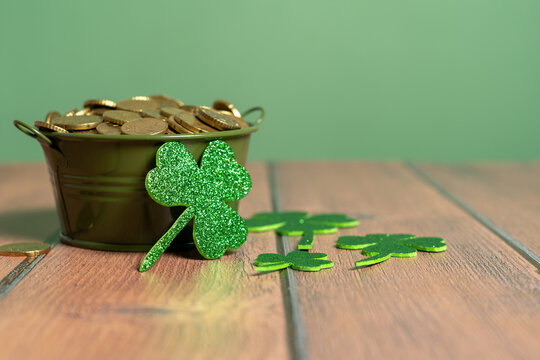 Pot full of coins next to several shamrocks on a wooden table and a light green background. St. Patrick's Day Celebration. High quality photo