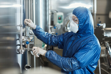 Worker wearing protective suit and mask operating equipment at chemical factory