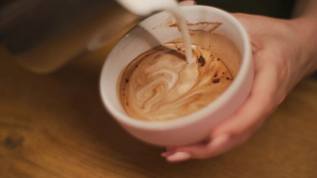 Hands of a barista making latte art in a coffee shop. The barista pours hot milk into the coffee and draws a picture.Close up