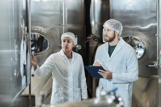Two workers wearing lab coats in food factory workshop