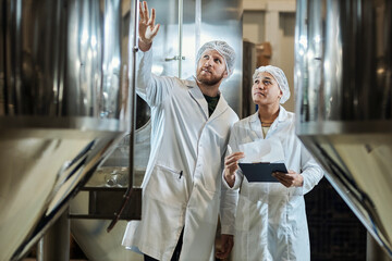 Two workers wearing lab coats inspecting equipment at food factory