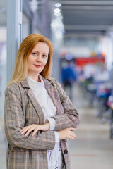 a business woman with long blondes in a plaid jacket stands in the office. 