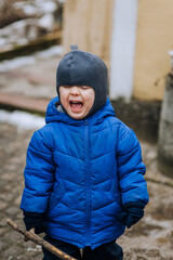 Naughty, screaming boy, child crying while standing outdoors. Close-up photography, emotions, childhood.