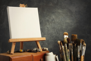 Artistic equipment in a artist studio: empty artist canvas on a wooden easel, paint tubes and paint brushes - used artistic paintbrushes for painting with oil or acrylic paints. - 573346890