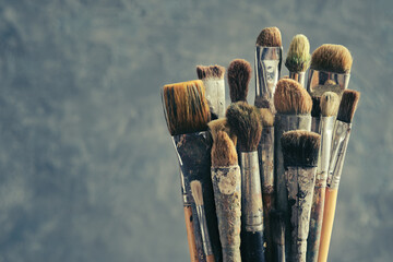 Used paint brushes on gray background. A bunch of brushes for painting with oil and acrylic paints. Artist paintbrushes in a artist studio.
