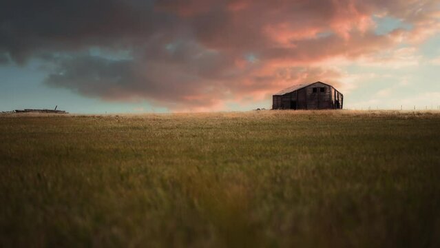 Epic sunset over an old abandoned bard in the green field. Slow motion. 
