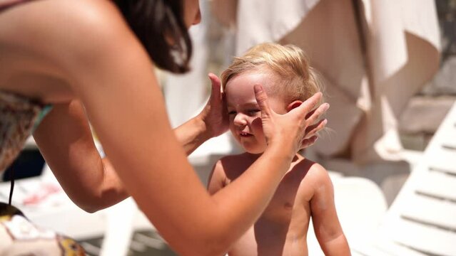 Mom smears sunscreen on the face of a little girl sitting on a sun lounger