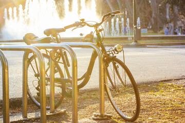 Classic two-wheeled bike parked in a bicycle parking lot in a city park on a sunny day at sunset in...
