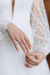 Obraz na płótnie Canvas A close-up photo of a wedding ring on the bride's finger. The bride is holding a wedding ring against the background of a white dress