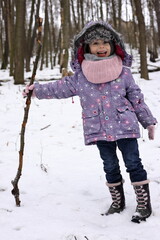 A child walks in the snow with a stick. Activity for winter holiday. Happy little girl enjoying the free time.