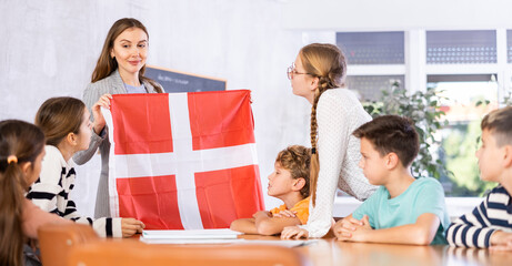 Fototapeta na wymiar School teacher tells students about Denmark and holds a Denmark flag in her hands.