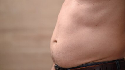 Man hits himself on stomach and takes folds of fat on his stomach, excess weight.