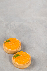 Two Round tartlets with tangerine cream and curly tangerine jelly. Light grey background. Copy space