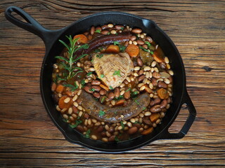 French Cassoulet, a meat and beans stew, in a cast iron skillet, on a rustic wooden table