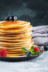 Delicious pancakes, with fresh blueberries, raspberry and maple syrup or honey on a dark background