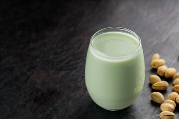 Organic pistachio milk in glass and pistachios on a dark green background. Non dairy alternative milk. Copy space