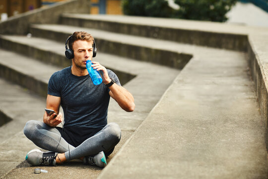 Young handsome men resting after jogging in the city and drink water from bottle and I listen to music through headphones