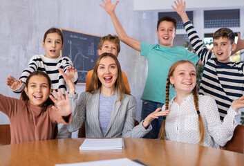 Group portrait of excited tween schoolchildren around positive young female teacher in classroom