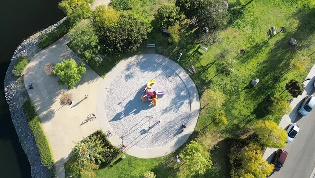 aerial view of a park with lake, fountain, playground with people on bicycles in a late afternoon day