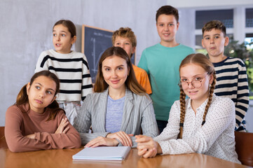 Fototapeta premium Portrait of friendly positive group of pupils with female teacher sitting in schoolroom