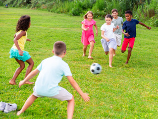 Obraz premium International group of active tweenagers having fun together outdoors, playing football on green grass in summertime