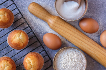Overhead view of baked muffins, eggs and wooden rolling pin on flour dusting