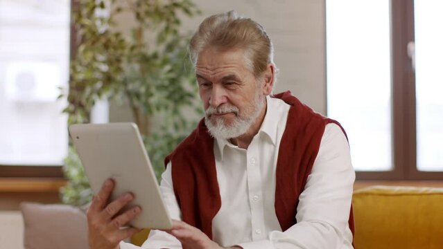 Internet and elderly people. Positive senior bearded man web surfing on digital tablet in social media, free space