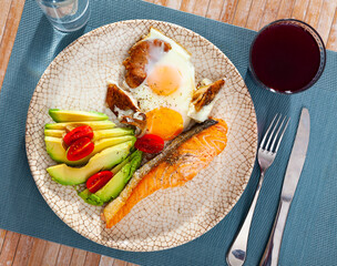 Grilled salmon fillet garnished with fried egg with mushrooms, fresh avocado and tomato