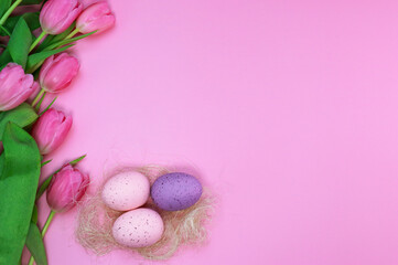 Obraz na płótnie Canvas flat lay pink Easter background with tulips and colourful eggs 