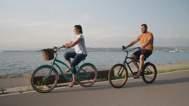 Caucasian couple riding bicycles relaxed on the coastal route and enjoying a view of the beautiful blue sea, tracking shot.