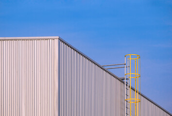 Corrugated iron Industrial Building Wall with cylinder Ladder against blue sky Background, perspective side view with copy space