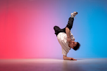 dancer doing acrobatic trick and dancing breakdance in neon red and blue lighting, young guy stands...