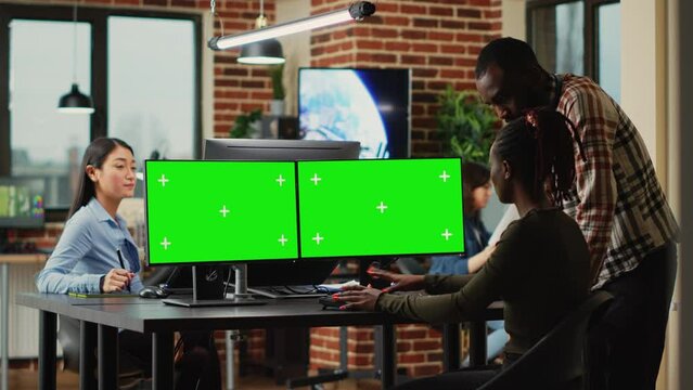 African american workers using greenscreen display on monitors, cheking quality of isolated mockup template. Team of office employees working with blank chroma key copyspace at creatve agency.