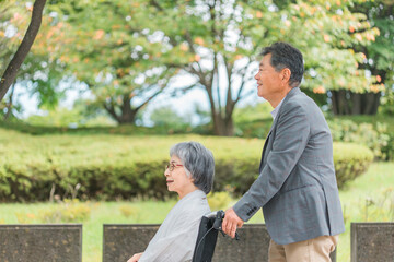 車椅子に乗って散歩する日本人の高齢者夫婦
