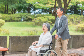 車椅子に乗って散歩する日本人の高齢者夫婦
