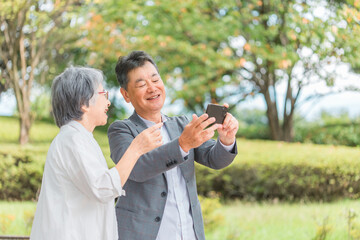 公園・旅行先で一眼レフカメラを使う高齢者夫婦（シニア・男女）  © buritora