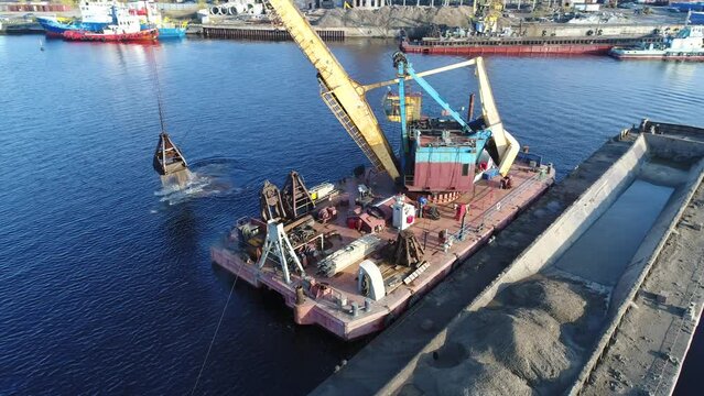 Aerial view. The dredger is working. Extraction of river sand by a special floating crane. A dredging machine takes sand from the bottom of the river and loads it onto a barge.  