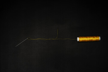 A needle with yellow thread threaded together with a spool of the same material on a black background