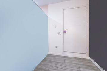 Entrance hall of an empty apartment with one sky blue wall, one gray wall, white wooden entrance door and gray wooden floors