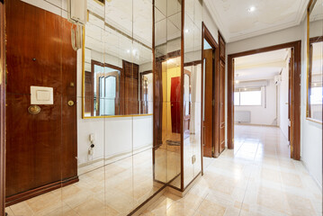 Entrance hall of an empty apartment with a wall covered in mirror panels and a long corridor leading to an empty room