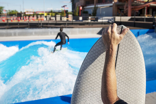 A surfer holding his wet board waiting his turn in the wave pool